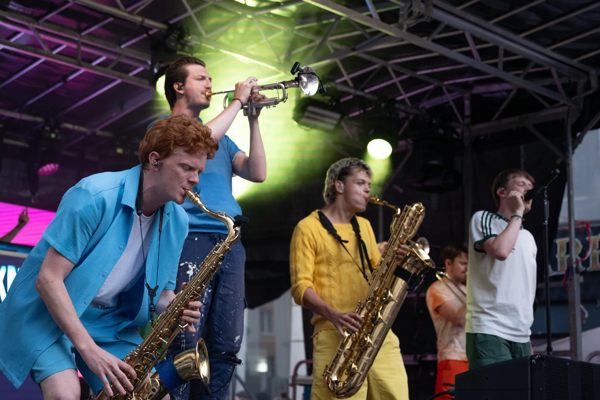 Eine Band spielt auf einer Buhne vor Publikum: Zwei Saxofonisten, ein Trompeter und ein Sanger performen live.