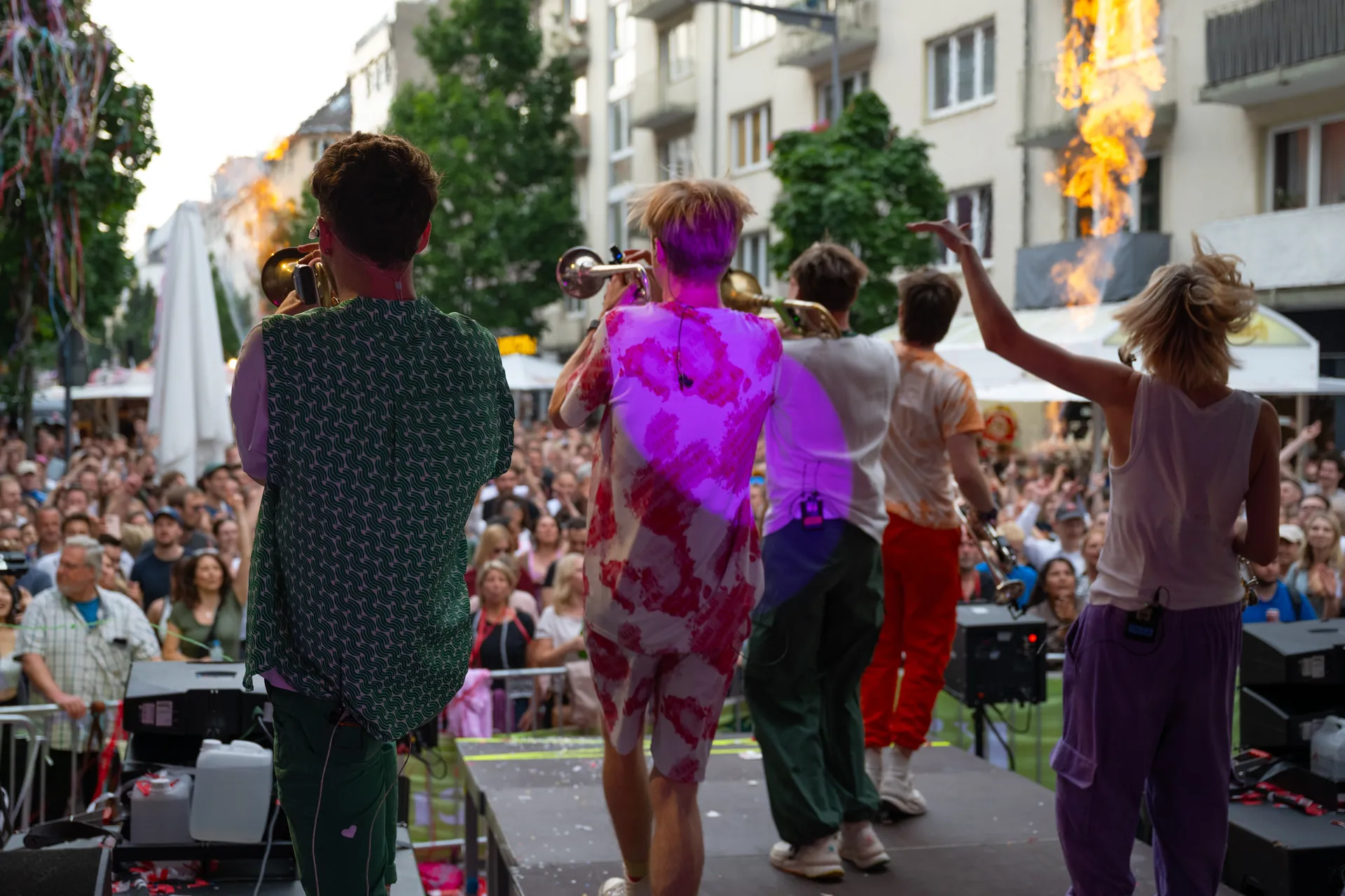 Funf Musiker stehen mit Trompeten auf einer Buhne und spielen vor grossem Publikum im Freien.