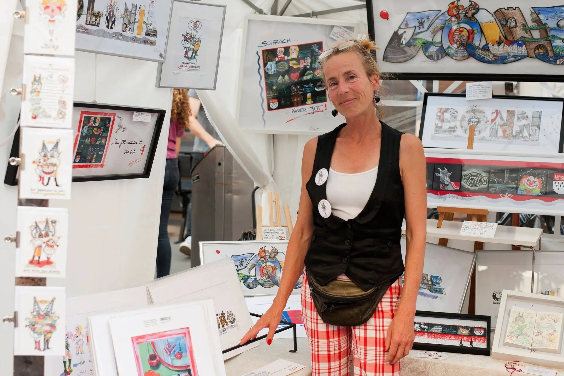 Eine Kunstlerin prasentiert ihre bunten Zeichnungen und Drucke auf einem Kunsthandwerkermarkt im Freien.