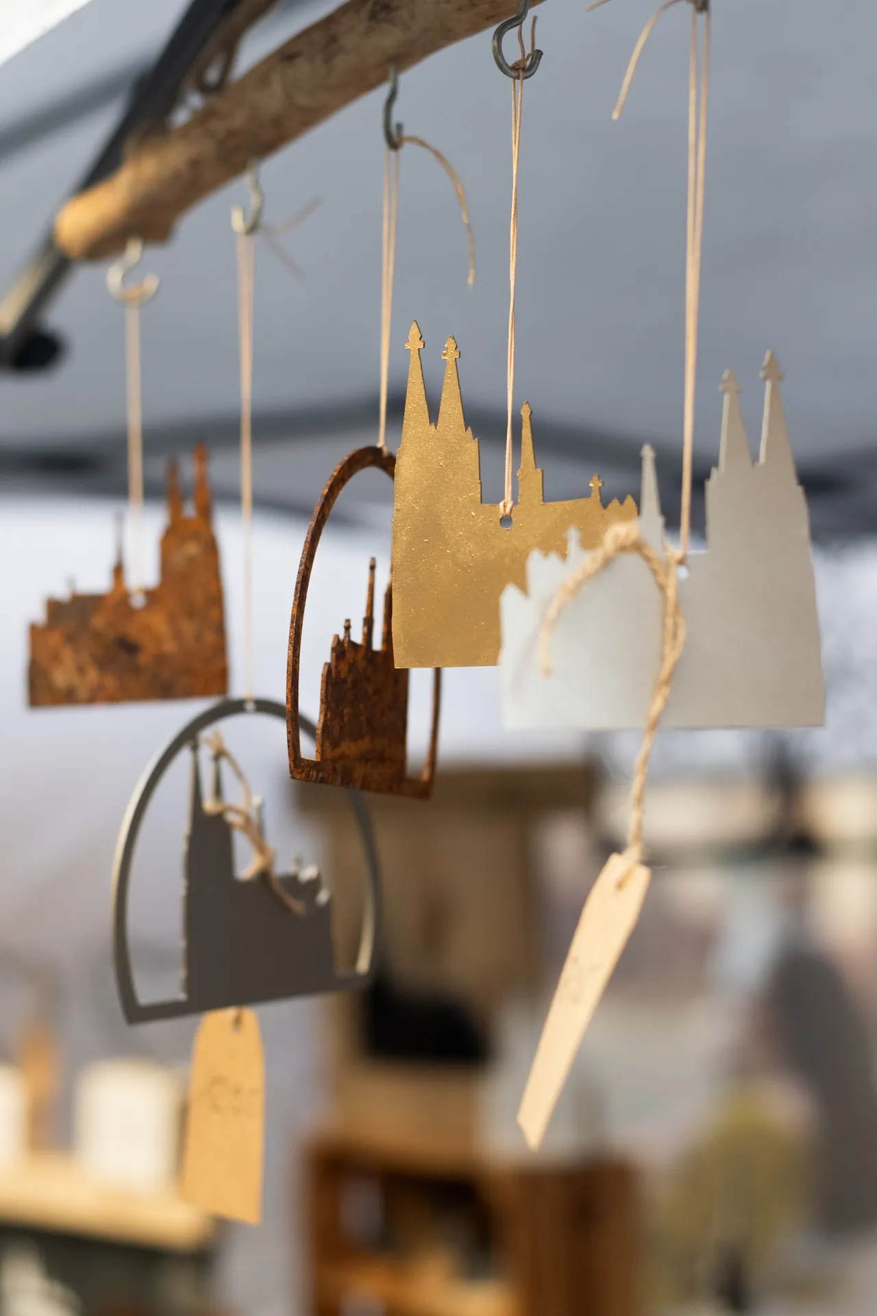 Mehrere Skyline-Anhanger der Stadt Koln in unterschiedlichen Farben und Materialien hangen an einer Holzstange, die mit Haken befestigt ist.