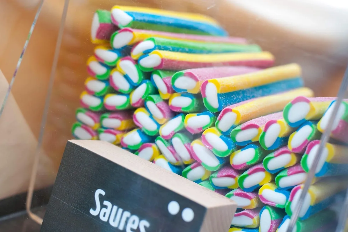 Ein Haufen bunter, saurer Regenbogen-Stangen, die in einem Behalter gestapelt sind, neben einer kleinen Tafel mit der Aufschrift Saures.