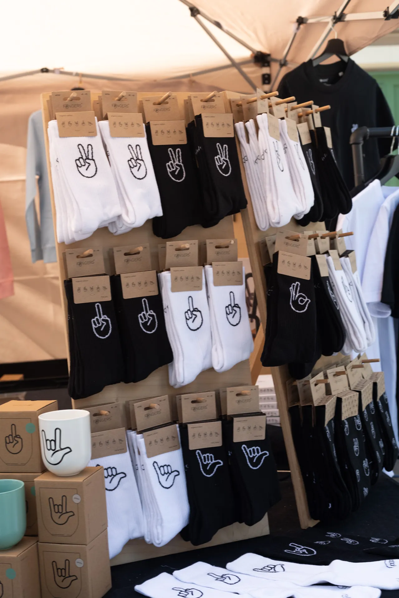 Auf einem Verkaufsstand werden schwarze und weisse Socken mit verschiedenen Handmotiven sowie Tassen und Kartons mit ahnlichen Motiven angeboten.